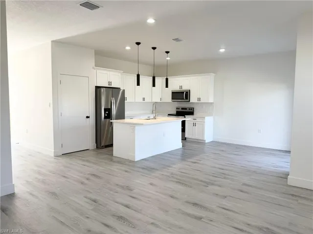 Kitchen with hanging light fixtures, appliances with stainless steel finishes, white cabinets, a center island with sink, and backsplash