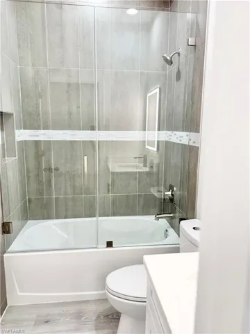 Full bath featuring wood finished floors, bath / shower combo with glass door, and vanity
