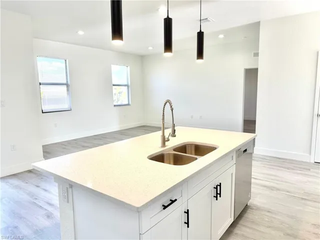 Kitchen featuring light stone counters, hanging light fixtures, a kitchen island with sink, white cabinets, and light wood finished floors