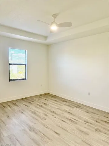 Unfurnished room with light wood-type flooring, a ceiling fan, and a raised ceiling