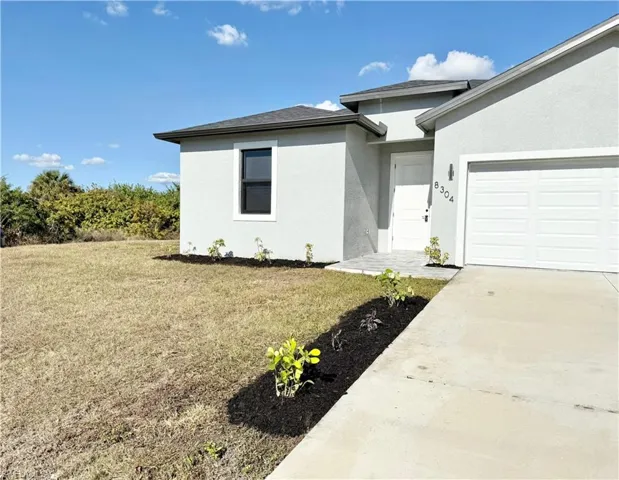 Property entrance featuring a lawn, stucco siding, an attached garage, and concrete driveway