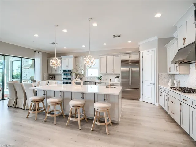 Kitchen featuring hanging light fixtures, a center island with sink, a kitchen bar, light hardwood / wood-style flooring, and stainless steel appliances