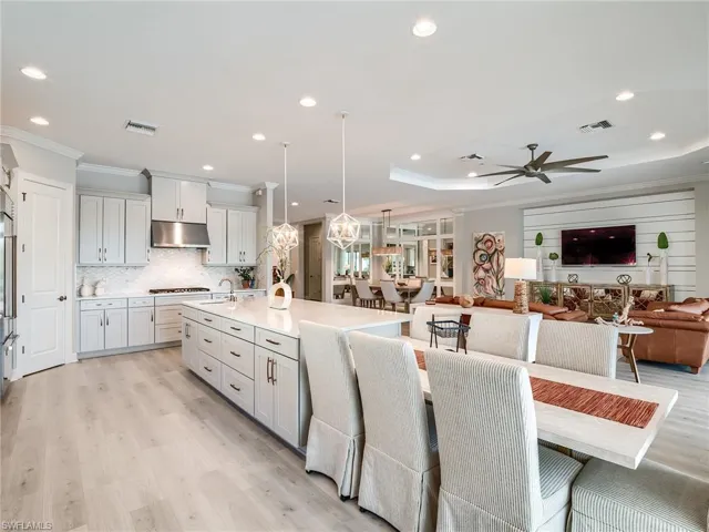 Kitchen with decorative backsplash, an island with sink, hanging light fixtures, crown molding, and light wood-type flooring