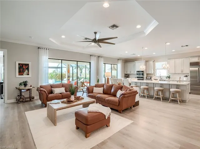 Living room with a raised ceiling, ceiling fan, light hardwood / wood-style flooring, crown molding, and sink