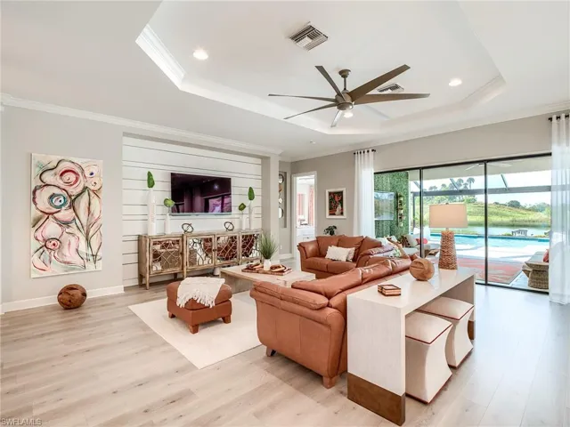 Living room with light hardwood / wood-style flooring, ornamental molding, ceiling fan, and a raised ceiling