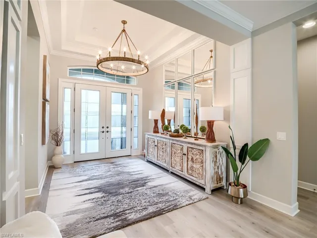 Foyer entrance featuring french doors, light hardwood / wood-style floors, a notable chandelier, and a raised ceiling
