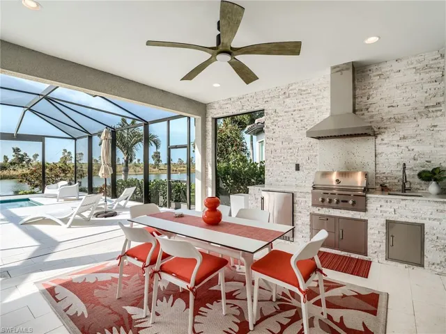 View of patio featuring ceiling fan, glass enclosure, area for grilling, sink, and a water view
