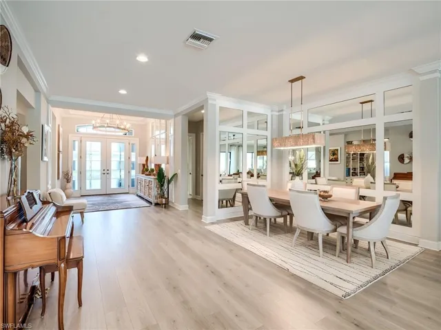 Dining room with french doors, light hardwood / wood-style flooring, crown molding, and an inviting chandelier