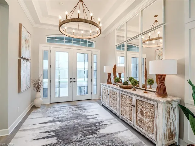 Doorway to outside with hardwood / wood-style flooring, a chandelier, a tray ceiling, crown molding, and french doors