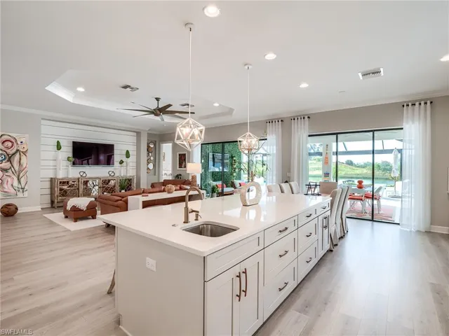 Kitchen with an island with sink, hanging light fixtures, sink, light wood-type flooring, and white cabinets
