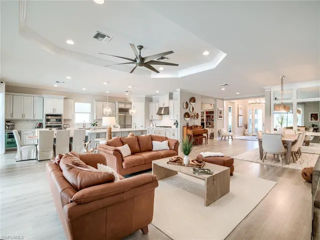 Living room featuring a raised ceiling, ceiling fan with notable chandelier, light hardwood / wood-style floors, and plenty of natural light