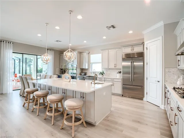 Kitchen featuring decorative backsplash, a center island with sink, a breakfast bar, decorative light fixtures, and appliances with stainless steel finishes