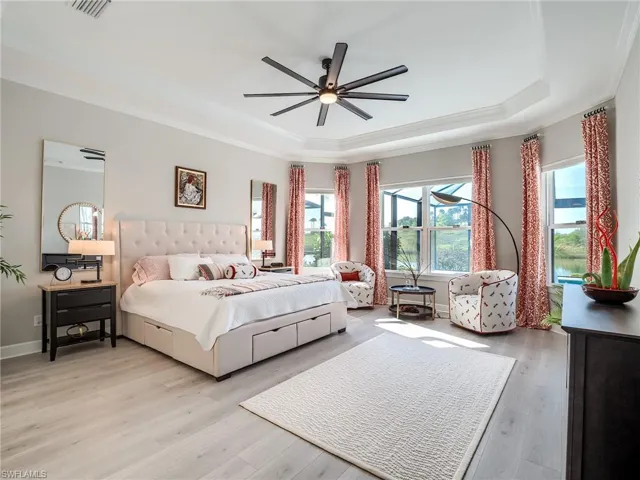 Bedroom with ornamental molding, light hardwood / wood-style flooring, a raised ceiling, and ceiling fan