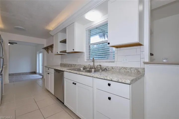 Kitchen with white cabinetry, light tile patterned floors, a textured ceiling, stainless steel dishwasher, and sink