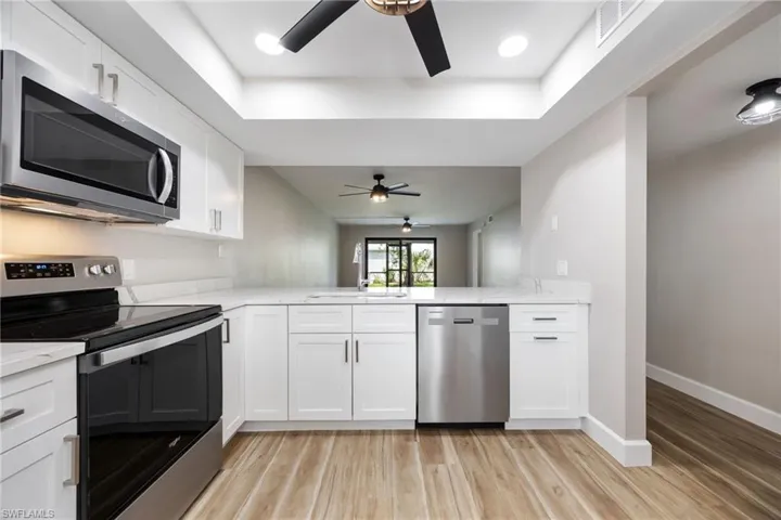Kitchen featuring stainless steel appliances, ceiling fan, light stone counters, light wood-style floors, and recessed lighting