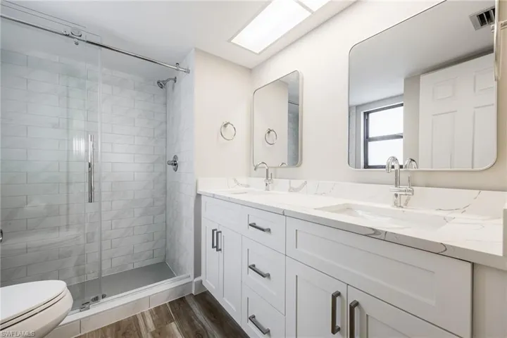 Bathroom featuring a stall shower, double vanity, and wood finished floors