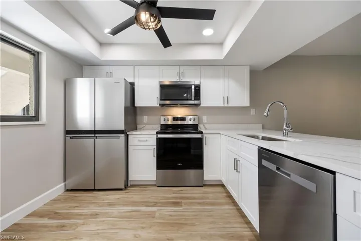 Kitchen with stainless steel appliances, a raised ceiling, recessed lighting, light wood-style flooring, and white cabinetry