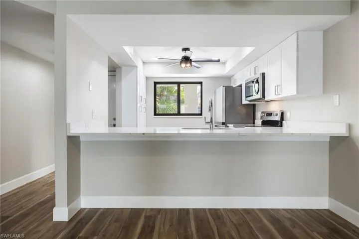 Kitchen with a peninsula, dark wood-type flooring, stainless steel microwave, range, and white cabinets