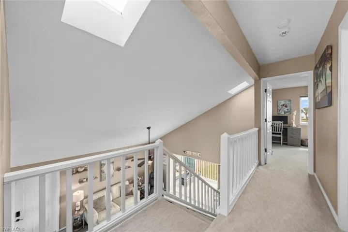 Corridor with light colored carpet and lofted ceiling with skylight