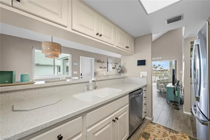 Kitchen with white cabinetry, stainless steel appliances, sink, hanging light fixtures, and light stone counters