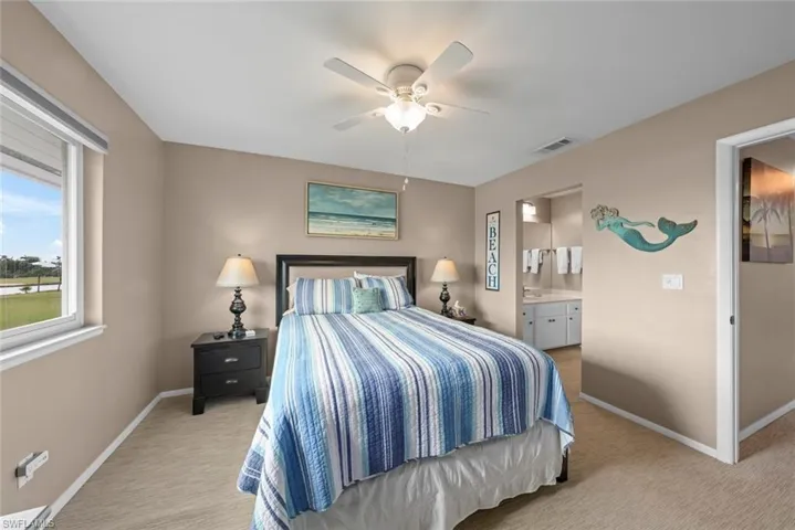 Bedroom with ceiling fan, connected bathroom, and light colored carpet