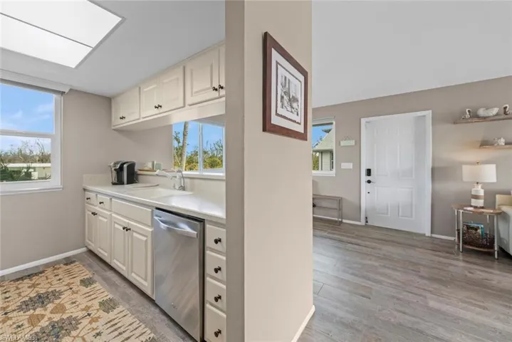 Kitchen featuring white cabinetry, a skylight, sink, stainless steel dishwasher, and light hardwood / wood-style flooring