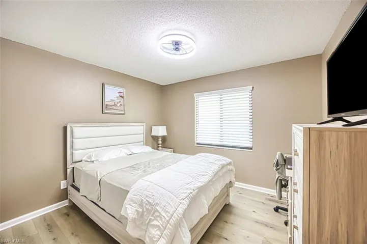 Bedroom with light wood-style floors, baseboards, and a textured ceiling