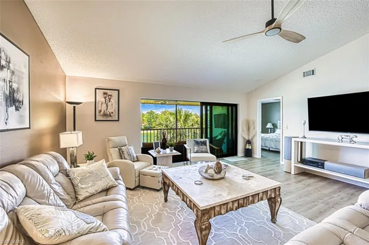 Living area featuring a textured ceiling, vaulted ceiling, ceiling fan, and light wood finished floors