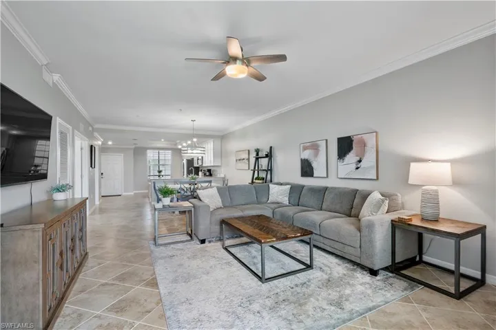 Living room with crown molding, a ceiling fan, light tile patterned flooring, and a chandelier