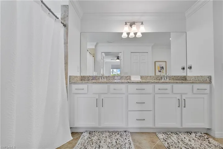 Bathroom with crown molding, double vanity, curtained shower, and light tile patterned floors