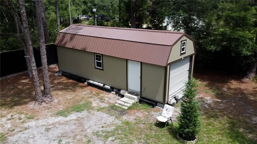 Detached utility building featuring a gambrel metal roof, olive green siding, and a roll-up garage door