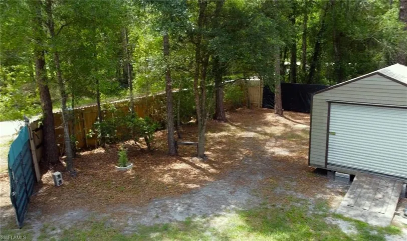 Backyard featuring a shed with a roll-up door and ramp, mature trees, wood fencing, and a gravel and grass ground cover