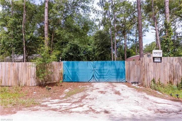 Gated entrance with a wood privacy fence and a gravel driveway, framed by mature trees