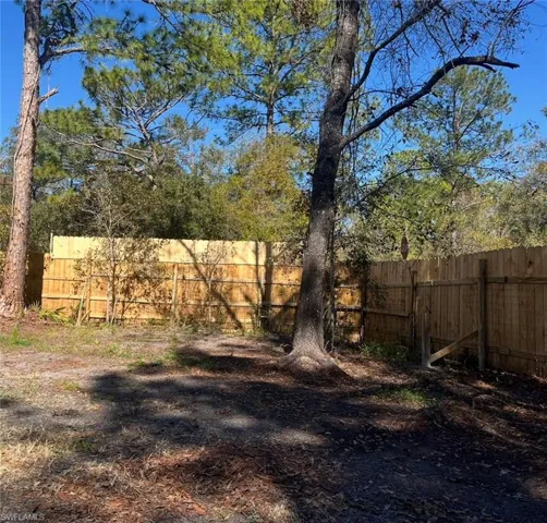 Expansive outdoor space featuring a wood privacy fence, mature trees, and natural ground cover