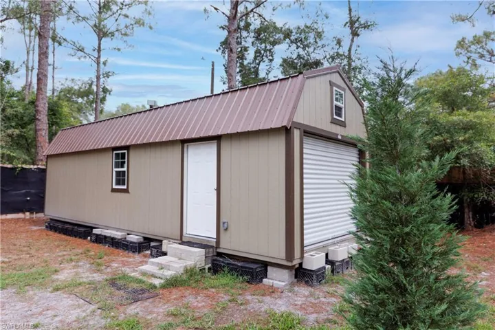 Detached utility building featuring a corrugated metal roof, light tan siding with brown trim, and a full-size roll-up garage door