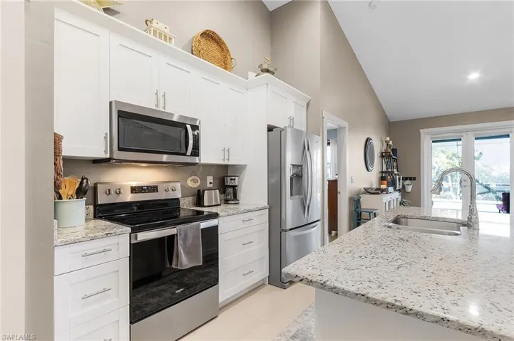 Kitchen featuring white cabinetry, appliances with stainless steel finishes, light stone countertops, and sink