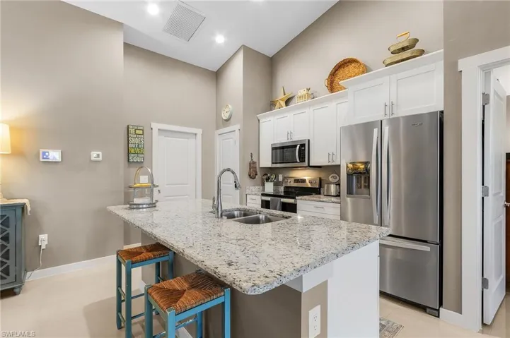 Kitchen with white cabinetry, light stone counters, a center island with sink, appliances with stainless steel finishes, and a kitchen breakfast bar