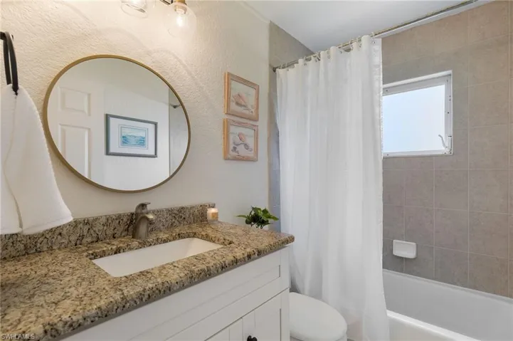 Bathroom featuring a vanity with a granite countertop and an undermount sink, a bronze-finish faucet, and a round wall-mounted mirror