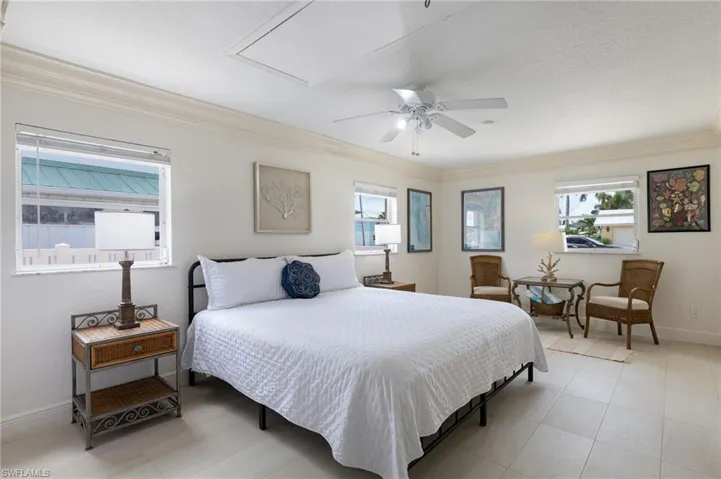 Spacious room featuring multiple windows, crown molding, a ceiling fan with integrated lighting, and light-toned square tile flooring