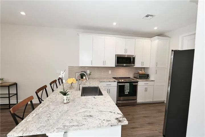 Kitchen featuring light stone countertops, stainless steel appliances, a kitchen bar, white cabinets, and dark wood-style flooring