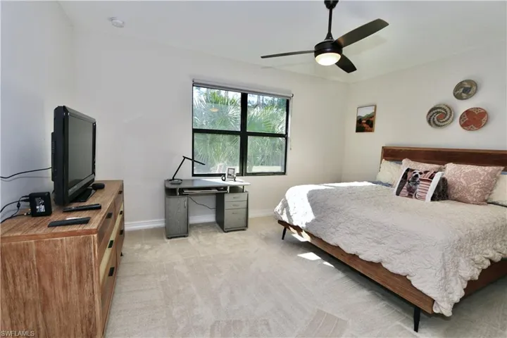 Bedroom with ceiling fan, light colored carpet, and a desk