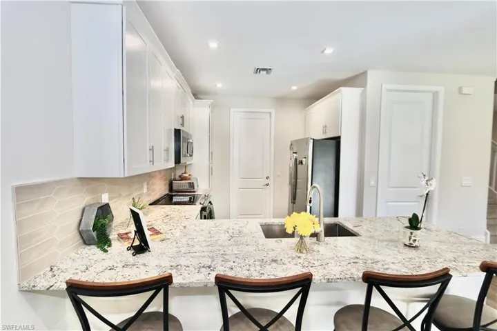 Kitchen featuring white cabinets, stainless steel appliances, light stone counters, decorative backsplash, and a breakfast bar area