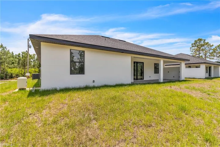 Rear view of property with a patio area, a lawn, stucco siding, and roof with shingles