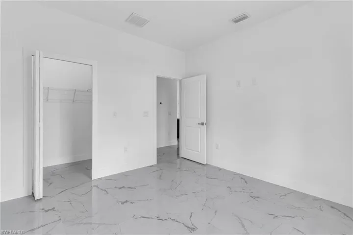 Unfurnished bedroom with a walk in closet and light marble finish flooring