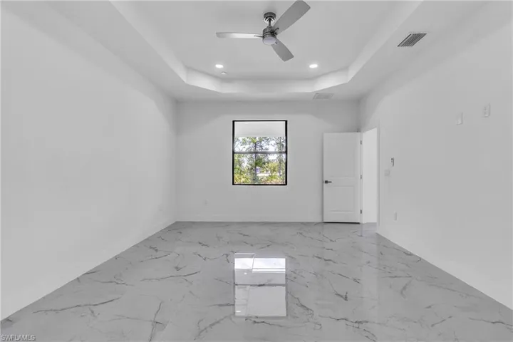 Unfurnished room with light marble finish floors, a tray ceiling, recessed lighting, and a ceiling fan