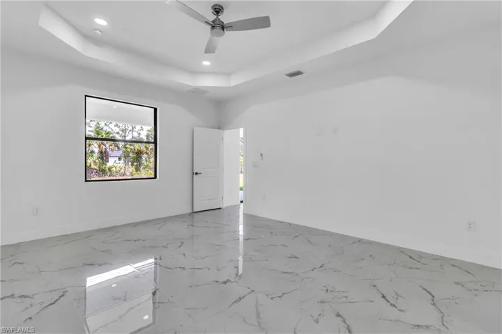 Empty room with light marble finish floors, a tray ceiling, recessed lighting, and ceiling fan