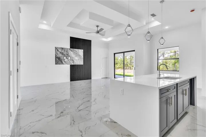 Kitchen with light marble finish flooring, pendant lighting, light stone countertops, open floor plan, and a kitchen island with sink