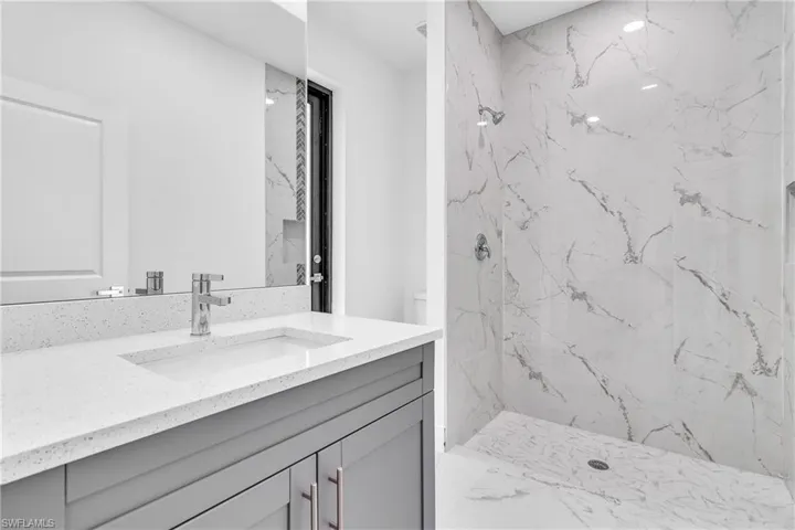 Bathroom featuring a marble finish shower, vanity, and light marble finish flooring