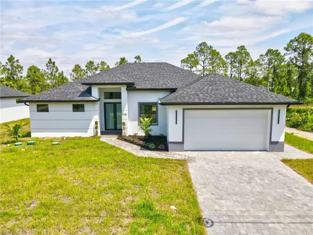 View of front facade featuring roof with shingles, decorative driveway, a front lawn, and stucco siding