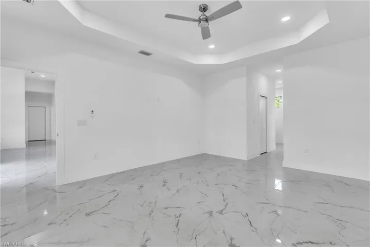 Unfurnished room with a raised ceiling, recessed lighting, light marble finish flooring, and ceiling fan